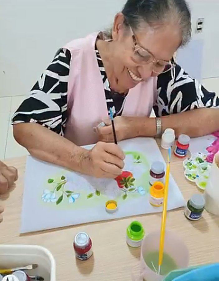 Participante sorrindo enquanto pinta flores em um pano de prato